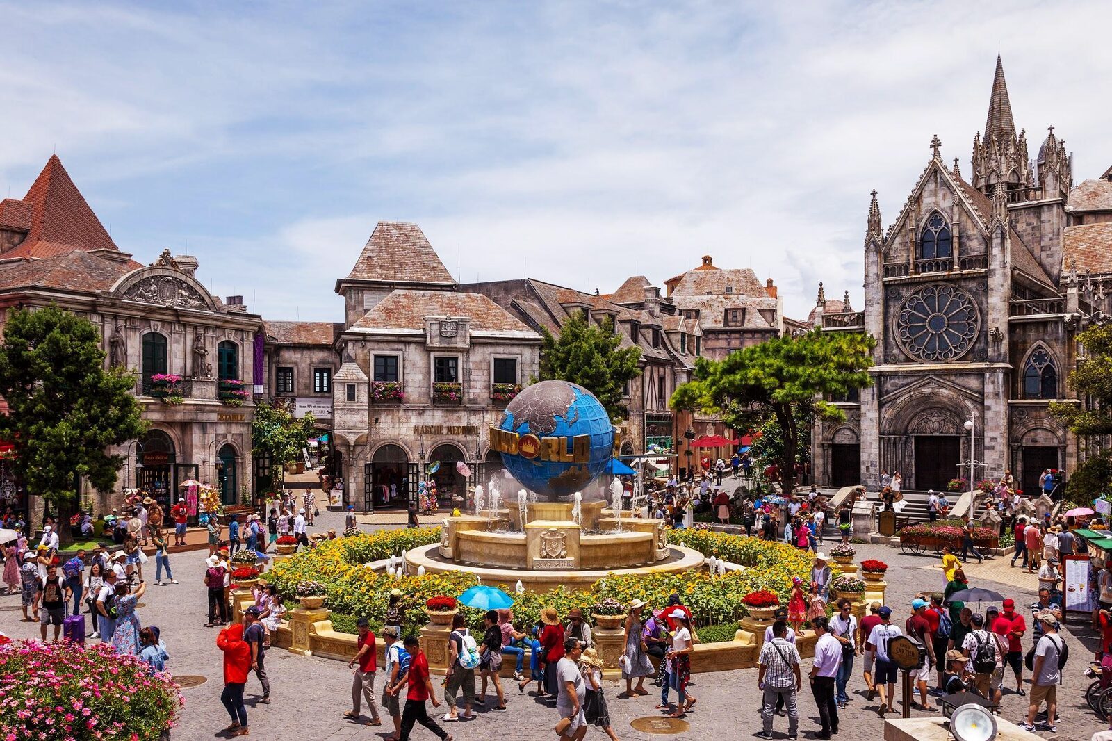 Visitors gather around the globe fountain in the French Village square at Sun World Ba Na Hills near Da Nang, with a Gothic-style cathedral facade in the background.