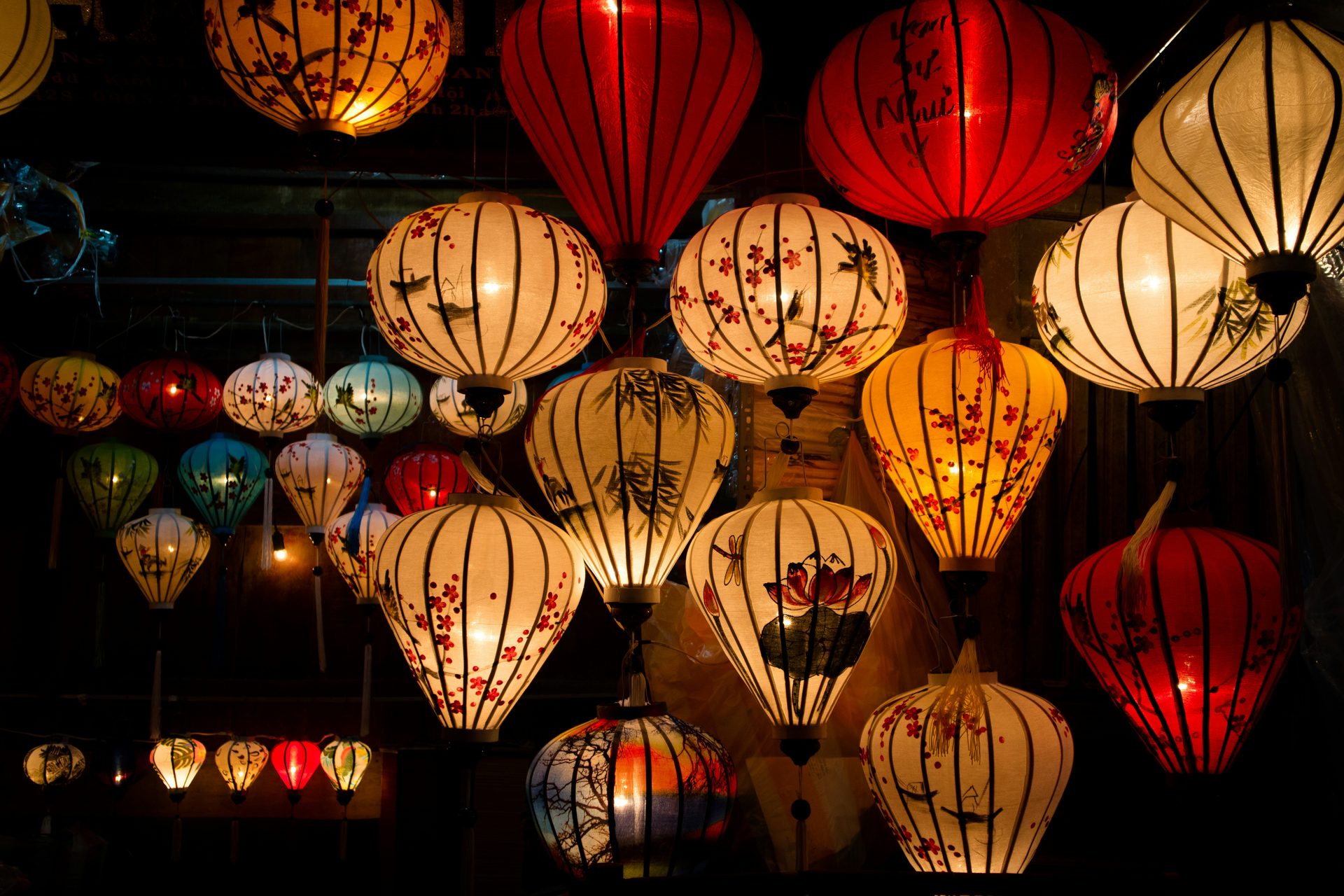 Rows of handmade silk lanterns in red, yellow, and blue glow above a street in Hoi An's Ancient Town at night.