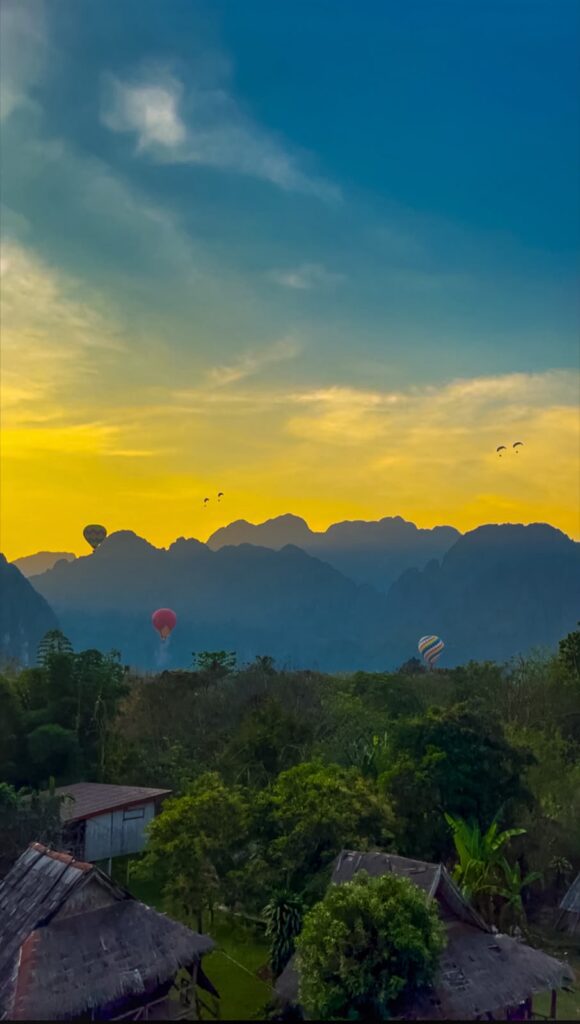 Hot air balloons and paragliders over the limestone karst mountains near Vang Vieng, Laos at dusk