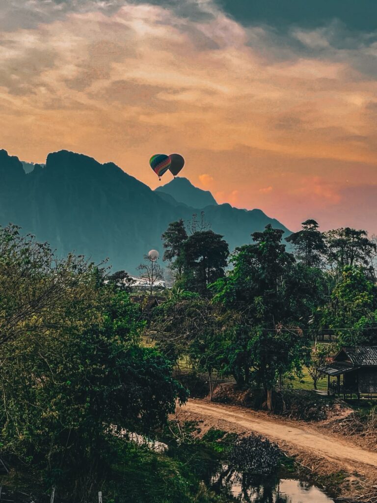 Two hot air balloons drifting together over misty limestone mountains at sunset near Vang Vieng, Laos