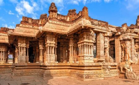 Close-up of an ancient Hampi temple pavilion with intricately carved stone pillars and a sculpted yali figure at sunset.