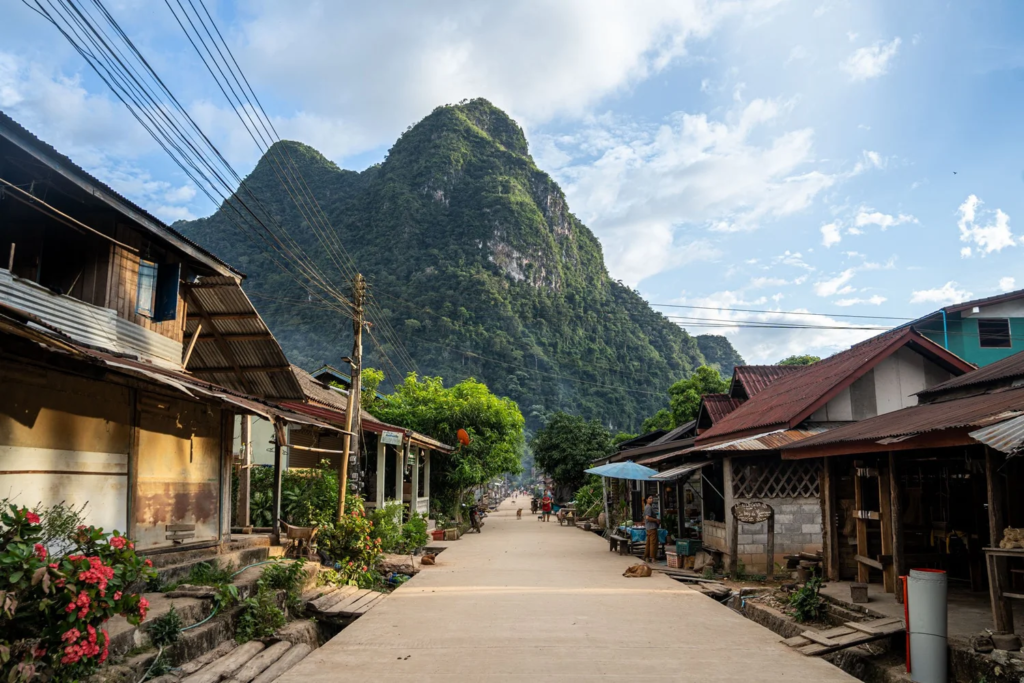 Quiet riverside village street in Muang Ngoi with dramatic karst mountains rising behind the houses, Laos