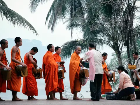 Buddhist monks in saffron robes collecting alms at dawn along the Mekong riverfront in Luang Prabang, Laos