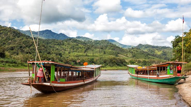 Traditional wooden slow boats moored on the Mekong River with forested hills behind, near Luang Prabang, Laos