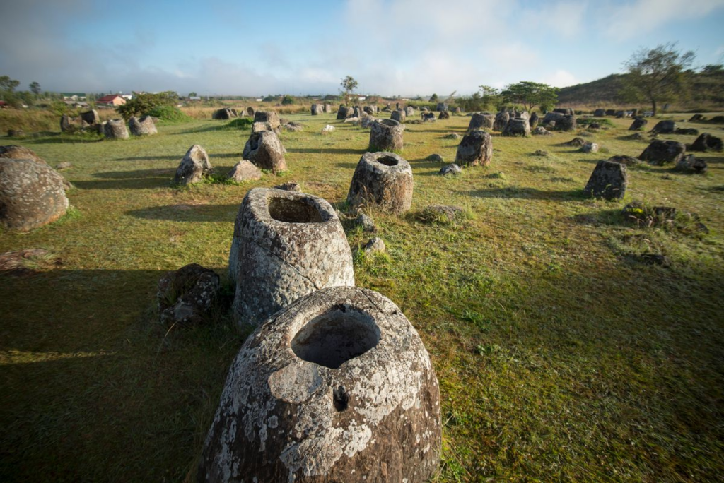 Ancient stone jars scattered across the grassy landscape of the Plain of Jars in Xieng Khouang, Laos