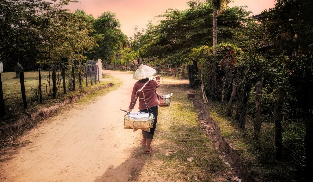 A local villager carrying baskets on a shoulder pole along a rural road in Laos
