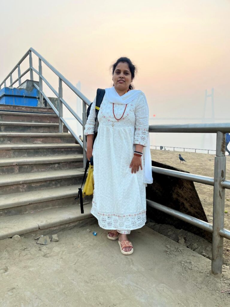 A traveller standing beside stone steps at a Varanasi ghat during a hazy Mahakumbh sunrise, the Ganges River in the background