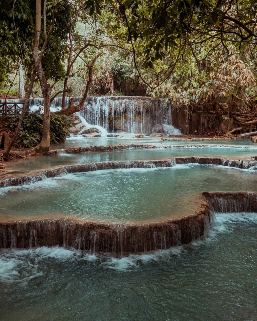 Turquoise cascading pools of Kuang Si Waterfall surrounded by lush forest near Luang Prabang, Laos